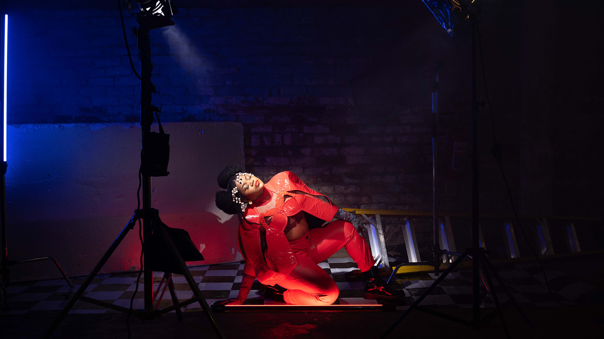 Busiswa kneeling with one knee while leaning back on one arm, sandwiched between two spotlights