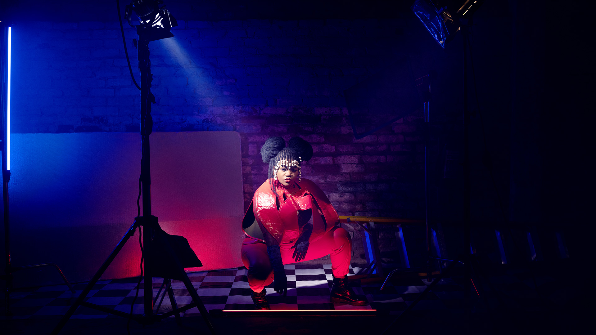 Busiswa crouching between two spotlights, dressed in red